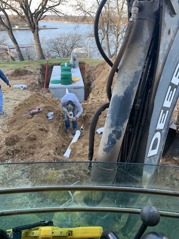 Lone Star crew connecting pipe to a new septic tank, seen from the backhoe cab