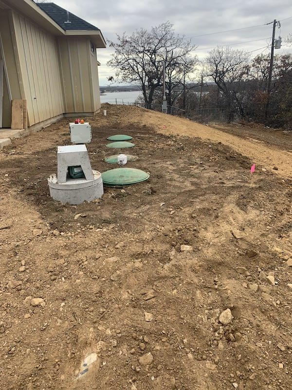 Aerobic septic system with control panel and spray head beside a home